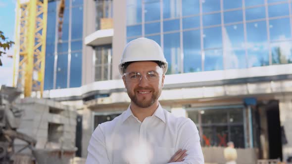 An Engineer in a White Shirt and Helmet Stands Against the Backdrop of a Modern Glass Building