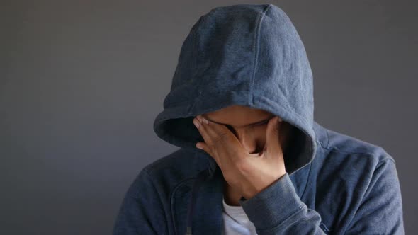 Sad Man in Hood Cover Face with Hands Isolated in Black