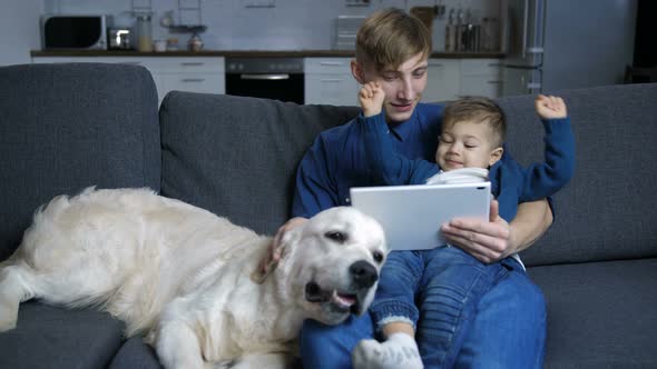 Dad and Son with Dog Watching Cartoons on Touchpad