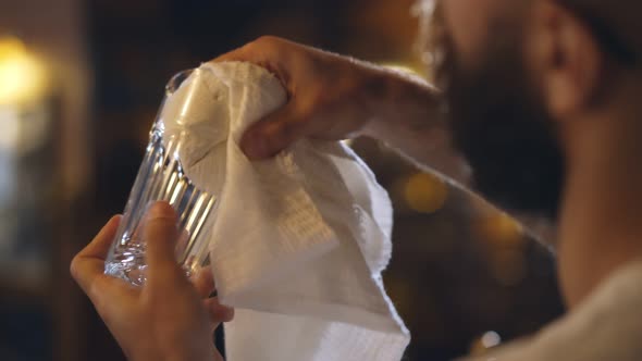 Bartender Rubbing Glass Standing at Bar Counter in Interior Pub