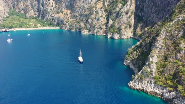aerial drone approaching a large sailboat docked in the bay of Butterfly Valley surrounded by turquo