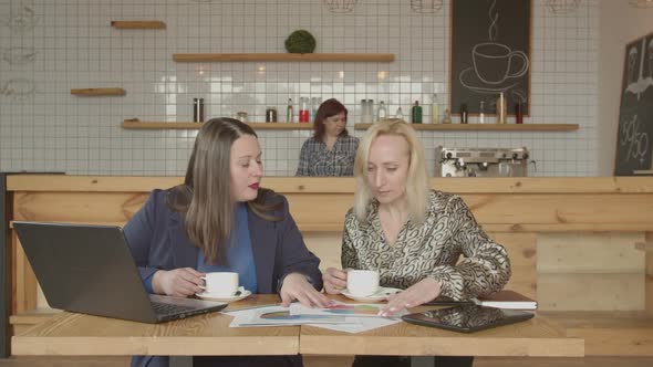 Two Females Drinking Coffee Working at Cafe Table