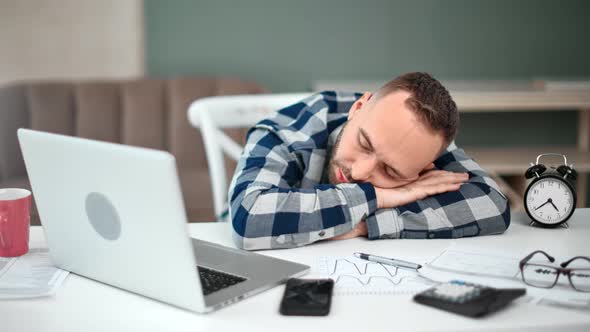 Man Sleeping on Desk at Workplace Surrounded By Paper Documents Laptop