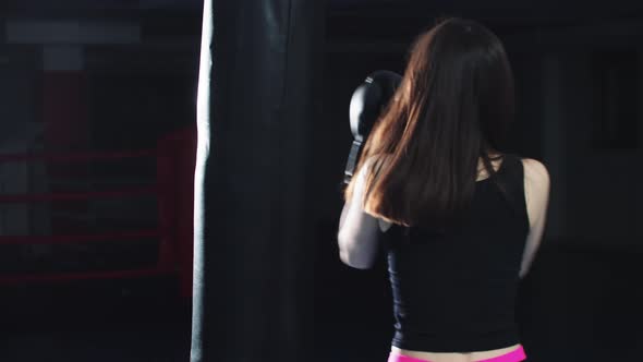 Young Woman with Long Hair Hitting the Punching Bag on the Boxing Ring