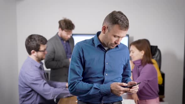 Man Is Checking E-mail By Cell Phone in Office in Conference Hall and Answering on Message