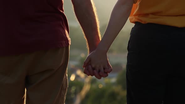 The man takes the woman's hand, clasping it tightly and crossing his fingers