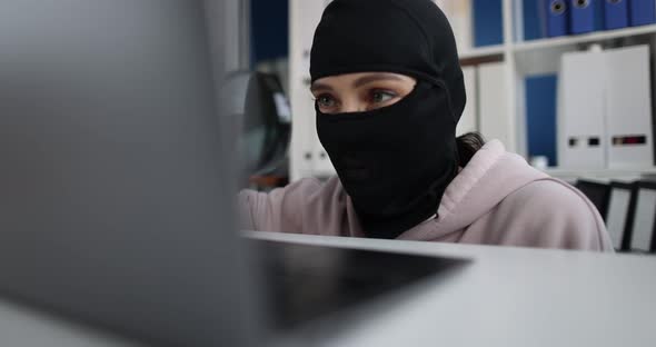 Swindler in Balaclava Looks Through Magnifying Glass at Computer Monitor