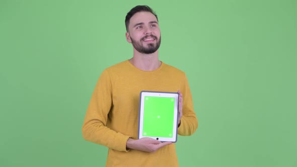 Happy Young Handsome Bearded Man Thinking While Showing Digital Tablet