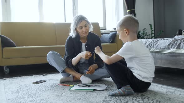 A Young Mother and A Baby Boy Are Sitting on the Floor, The Mother Is Teaching the Child To Draw