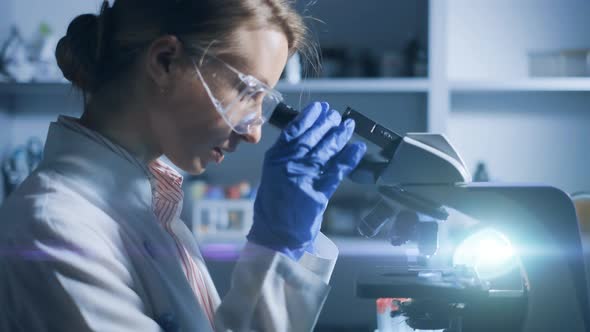 A Woman Scientist is Looking Into Microscope Biochemical Research alt