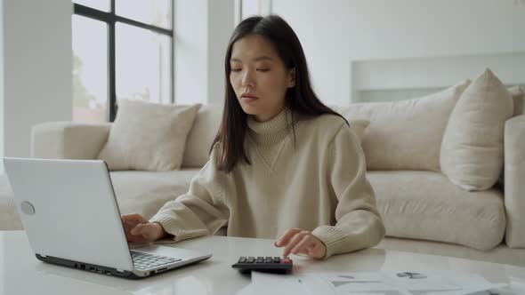 Asian Woman with Laptop and Calculator in the Living Room