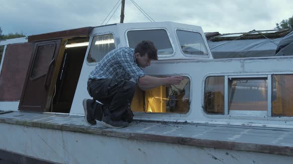 Carpenter scraping ring window seal on wooden liveaboard