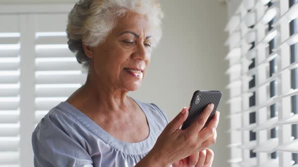 African american senior woman using smartphone and looking out of the window at home