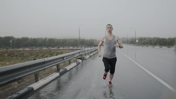 Sportsman of asian appearance, athletic build, runs along wet asphalt road highway