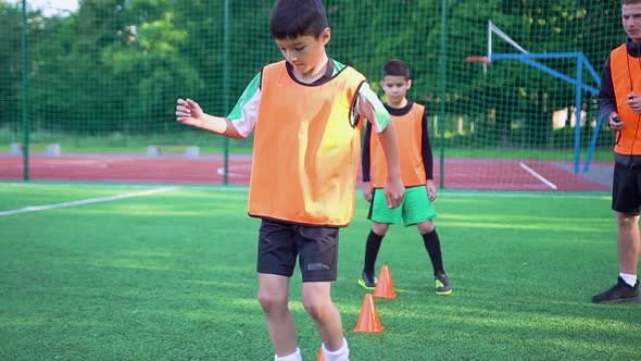 Teen Boys in Football Uniforms which Doing Running Exercises with Obstacles with Ball
