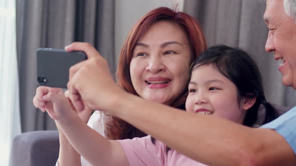 Senior Chinese, grandpa and grandma happy spend family time relax using mobile phone with young girl