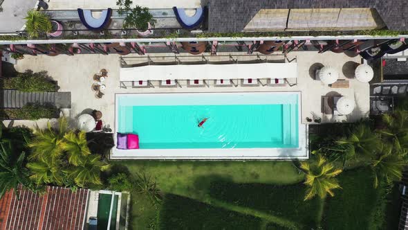 Woman in red swimsuit swimming at pool on Shore Amora Canggu Hotel pool in Bali, Indonesia, Aerial r