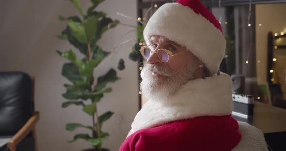 Closeup Portrait of Santa Claus Looking in Front of Him While Sitting at Home Against the Background