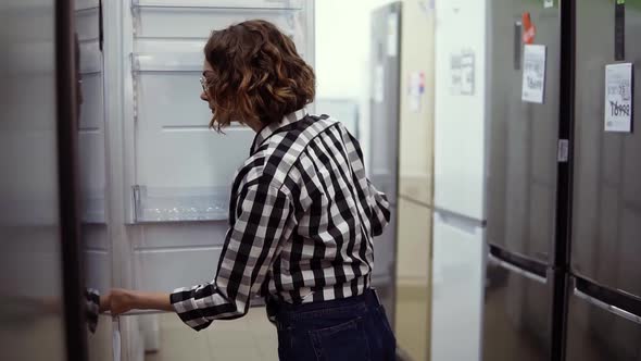 Cheerful Young Girl Selecting Domestic Refrigerator in Supermarket
