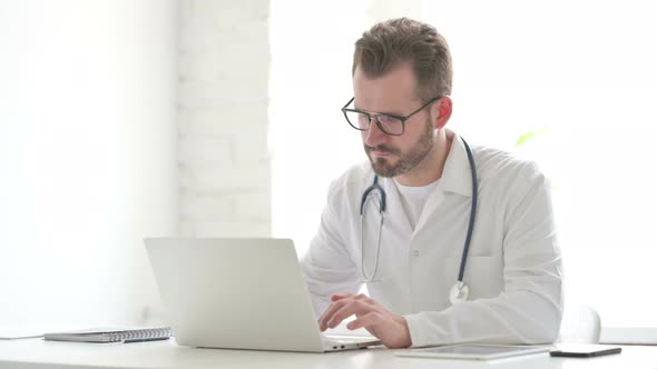 Doctor Looking at Camera While Using Laptop in Office