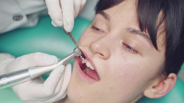 A dentist is doing the removal of deposits on the teeth and whitening for the client