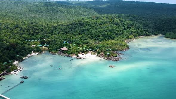 Aerial of white sand beach with straw huts along Forrest coastline with turquoise blue sea. Koh Rong