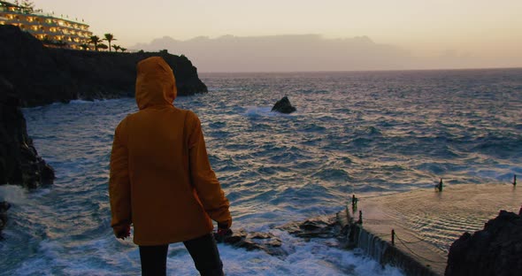 A Young Girl Watching the Ocean at the Edge on Top of a Rocky Seashore in 