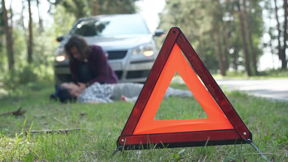 Closeup Red Emergency Road Sign with Blurred Anxious Man Crying and Dead Woman Lying at Background