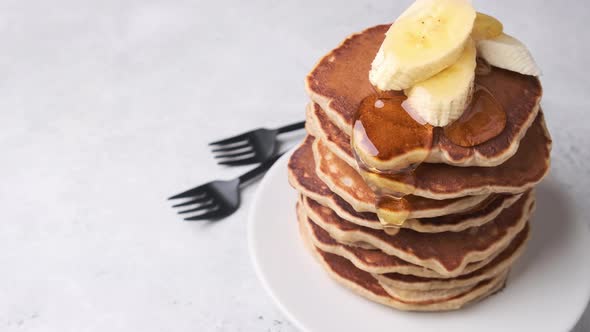 Banana pancakes with syrup on white plate, gray background.