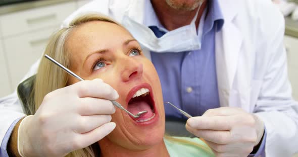 Dentist examining a female patient with dental tools