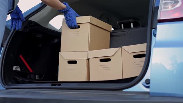 Courier in Protective Gloves Take Out Cardboard Box From Car Trunk