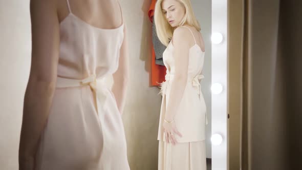 Young Caucasian Woman Trying on Elegant Dress in Dressing Room. Camera Moving Down, Wealthy Lady in