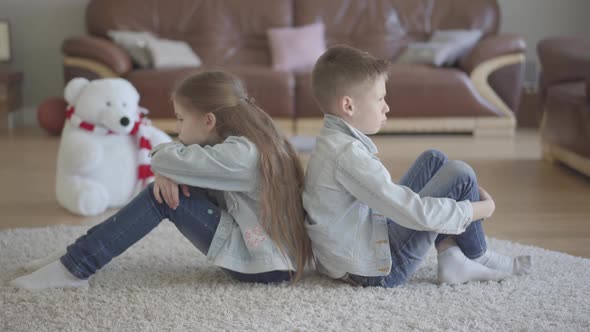 Twins Boy and Girl Sit on the Floor of Living Room Back To Back Angry To Each Other. Brother and