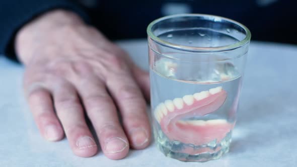 Close-up of a pensioner immersing his removed dentures into a glass of water.