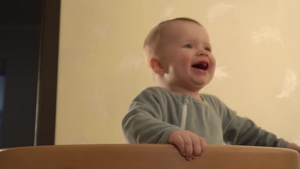 Happy Baby is Standing in the Crib with Soother in Mouth Ridding It Out and Jumping in Closeup