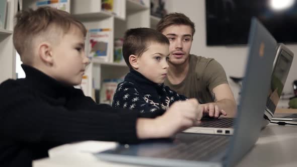 Young Attractive Male Teacher Showing Two Little Boys How to Use Gadgets Such As Laptop