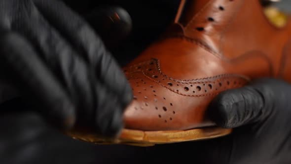 Closeup Hands of Shoemaker in Black Gloves Rubbing Paint on Toe Cup of Light Brown Leather Shoes