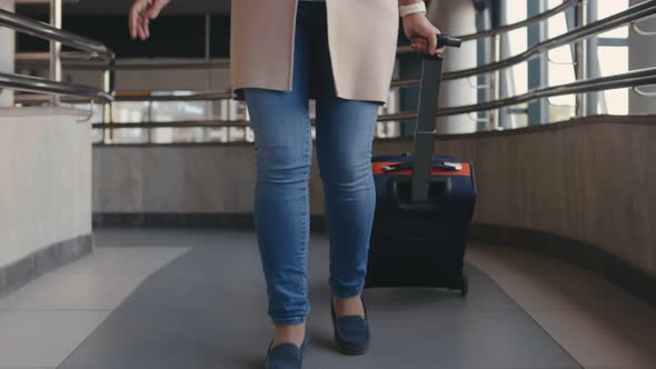 Caucasian Senior Woman Walks Through the Airport with Luggage Listening To Music By Headphones