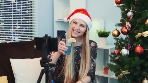 Close Up of Gorgeous Young Lady in Santa Hat Shooting a Video Blog By Smartphone at Home