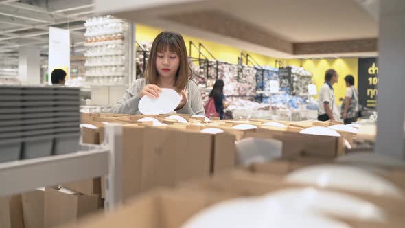 Young Asian woman rides shopping cart choosing new furniture in warehouse