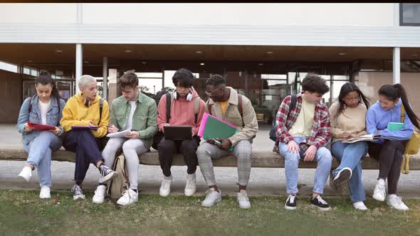 Multiracial University Students Working and Studying Together Sitting On Bench Outdoors In Campus