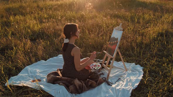 Young girl paints the picture on canvas in the countryside