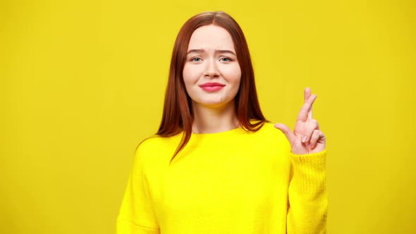 Portrait of Beautiful Worried Young Woman Crossing Fingers Posing at Yellow Background