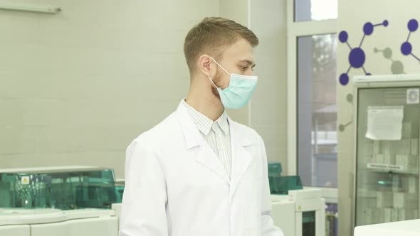 A Serious Lab Assistant Stands in the Middle of the Laboratory and Turns His Head Into the Camera