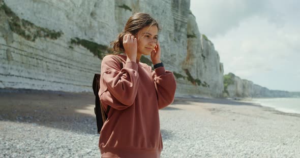 A Young Woman Walks Along a Pebbly Beach Past Sheer Chalk Cliffs