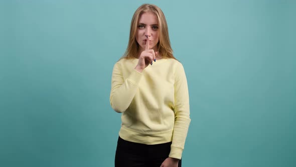 Smiling Girl Showing To Be Quiet with Finger Isolated Over Turquoise Background