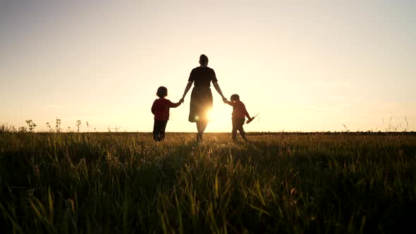 Silhouette of Young Family Mom and Two Brothers Twins Boys Walking Together to Sun on Open Air Field
