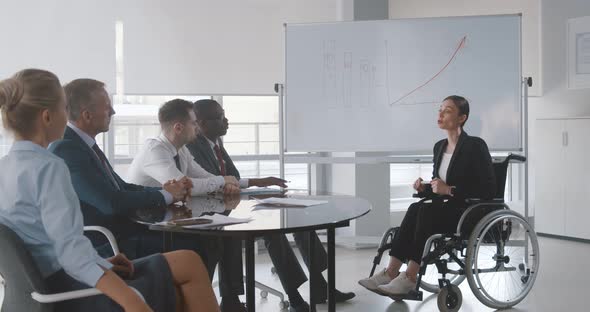 Young Woman in Wheelchair Teaching Group of Business People at Whiteboard in Office