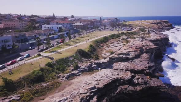 Aerial Drone shot of beautiful waterfront houses near a park and cliff with ocean waves crashing on