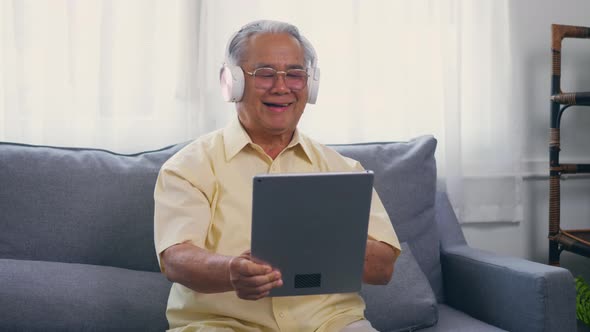 Old man grandfather smile relaxing wear headphones is listening to music using a digital tablet